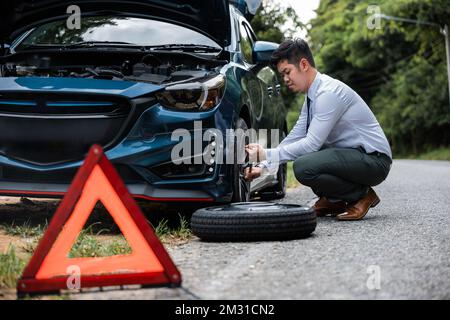 L'uomo d'affari asiatico auto rotta ha problemi con la ruota della sua auto Foto Stock