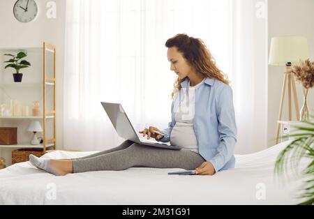 Focalizzata la giovane donna incinta sul congedo di maternità che lavora online a casa utilizzando il notebook. Foto Stock
