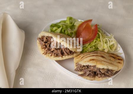 Arepas, cibo tipico venezuelano, a base di mais e ripieni di carne grattugiata su tovaglia bianca. Foto Stock