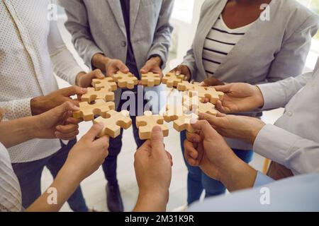 Gruppo di uomini e donne in piedi in cerchio e collegare identici pezzi di puzzle di legno. Foto Stock