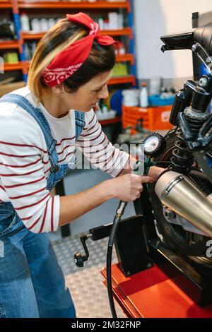 Donna meccanica che controlla la pressione d'aria degli pneumatici della motocicletta Foto Stock