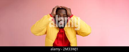 Vita-up sorpreso felice fortunato giovane afroamericano sopportato maschio in giallo giacca che tiene le mani testa sorridente impressionato gioiosamente ricevere impressionante Foto Stock