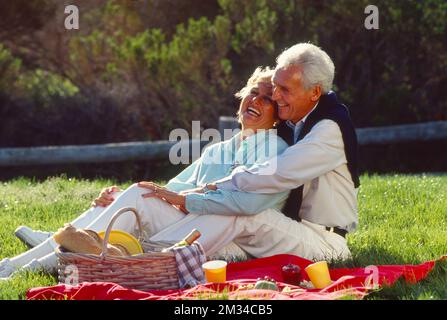 La coppia più anziana ride mentre si siede su una coperta da picnic nell'erba Foto Stock