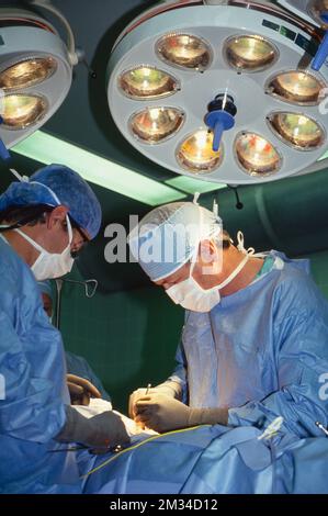 I medici eseguono interventi chirurgici sotto le luci in sala operatoria Foto Stock