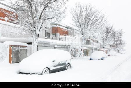 Strada residenziale completamente innevata con auto coperte di neve parcheggiate all'ingresso delle case. Paesaggio invernale. Spazio per il testo. Foto Stock