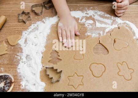 La bambina sta preparando il pan di zenzero in kitchen.View da above.Little mani con dought e farina, biscotti taglierini, spezie sul tavolo di legno. Foto Stock