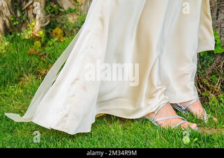 Un primo piano delle gambe di una donna in un abito di seta e scarpe blu con tacco alto in piedi su un'erba verde Foto Stock