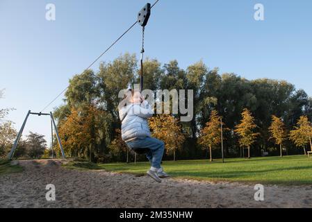 Divertimento all'aperto. Giovane ragazza in sella a un bungee appeso sul parco giochi. Autunno Foto Stock