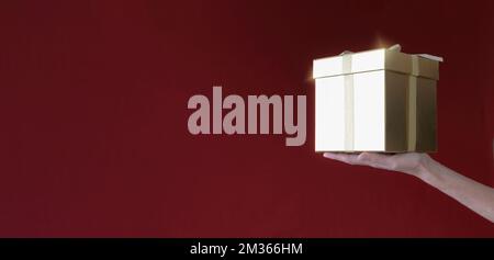 Una mano donna tiene una scatola regalo su uno sfondo rosso-bordeaux. copia banner spazio Foto Stock