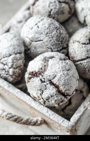 Chocolate chip cracked cookies close up. Wooden rustic box with fresh baked chocolate crinkle cookies in icing sugar. Vertical orientation Stock Photo