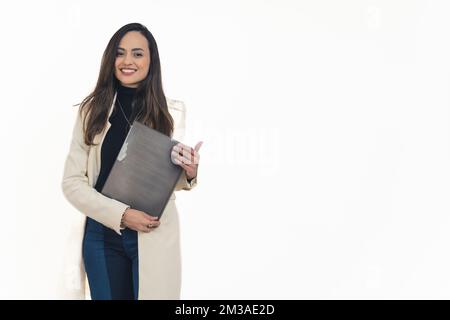 Donna d'affari latino-americana che indossa un cappotto in piedi di fronte alla fotocamera tenendo cartella documenti con entrambe le mani sorridente. Manager femminile. Titolare dell'azienda. Sfondo bianco copia spazio orizzontale studio shot. Foto di alta qualità Foto Stock