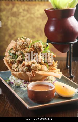 Un primo piano verticale di deliziose strisce di pollo croccanti accanto a una salsa e una fetta di limone su un piatto Foto Stock