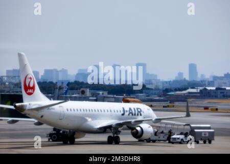 Tokyo, Giappone - 9 novembre 2022: Aereo della Japan Airlines sul asfalto con veicoli di supporto e skyline della città visibile attraverso la foschia Foto Stock