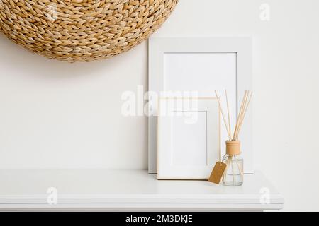 Cornici fotografiche vuote e diffusore reed su scaffale vicino alla parete bianca Foto Stock