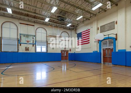 Palestra americana senza descrizione con pavimenti in legno e pareti blu imbottite che si trovano in una tipica scuola media o alta. Foto Stock