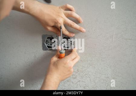 l'elettricista collega le prese ai fili elettrici sulla parete utilizzando un cacciavite, primo piano Foto Stock