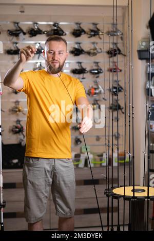 L'uomo sceglie la canna da pesca nel negozio di sport, il pescatore compra le canne da pesca Foto Stock