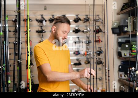 L'uomo del millennio sceglie la canna da pesca nel negozio di articoli sportivi, spazio copia Foto Stock