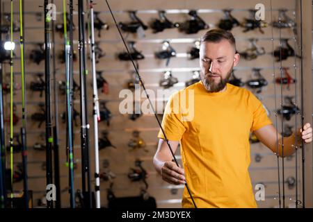 L'uomo del millennio sceglie la canna da pesca nel negozio sportivo, nel negozio di pesca, nello spazio copia Foto Stock