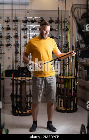 L'uomo sceglie la canna da pesca nel negozio sportivo, spazio copia Foto Stock