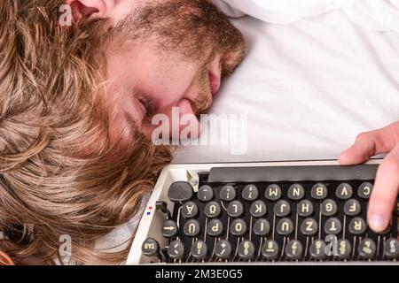 La macchina da scrivere usava una macchina da scrivere antiquata. Autore tousled capelli addormentarsi mentre scrive il libro. Addormentarsi in modo workaholic. Uomo con sonno da macchina da scrivere. Scadenza Foto Stock