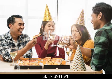 Un gruppo di amici asiatici diversi si riunisce per festeggiare il Natale con champagne e mangiare pizza a casa. Gioia di festa con amici o colleghi Foto Stock