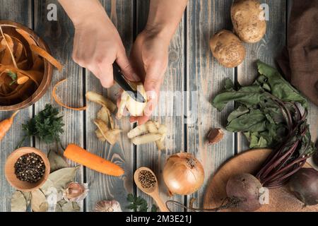 Donna irriconoscibile che sbuccia patate con coltello nero vicino a ciotola  di legno marrone con bucce di carote, ciotola piccola con pepperns, carota  sbucciata, cipolla Foto stock - Alamy