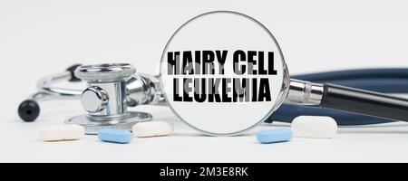 Medicina e concetto di salute. Su una superficie bianca ci sono pillole, uno stetoscopio e una lente d'ingrandimento all'interno del quale è scritto - leucemia a cellule capellute Foto Stock