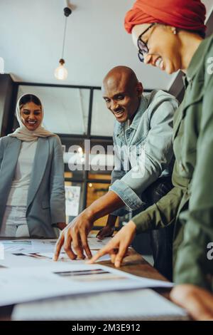 Designer d'interni felici che lavorano con tavolozze di colori in un ufficio moderno. Gruppo di imprenditori multiculturali che condividono idee innovative in un creativo Foto Stock