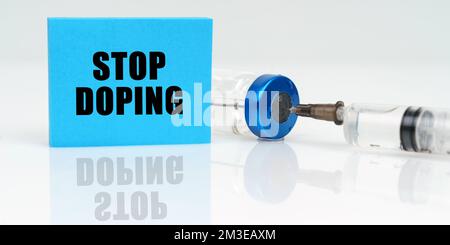 Concetto di medicina. Su una superficie riflettente bianca ci sono una siringa, un'iniezione e una placca blu che dice - Stop doping Foto Stock