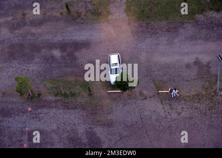 Auto parcheggiata da sola sotto un albero in un ampio parcheggio vuoto Foto Stock