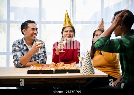 Un gruppo di amici asiatici diversity si diverte a parlare, a divertirsi insieme, a bere vino e a mangiare pizza durante la festa. Festa di nuovo anno, festa di compleanno, Foto Stock