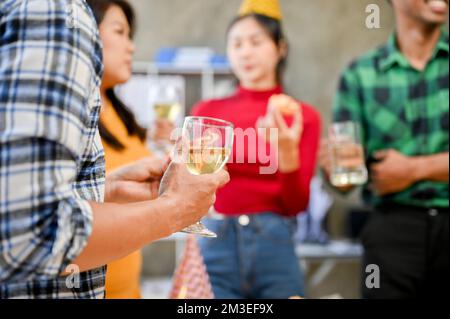 Immagine ritagliata, Un uomo in festa aziendale, tenendo un bicchiere di vino, godendo la festa sul suo posto di lavoro. Foto Stock