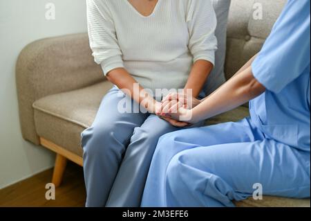 Medico curante e gentile o infermiera che tiene le mani di una donna anziana per confortare e sostenere la sensazione del paziente. immagine ritagliata Foto Stock