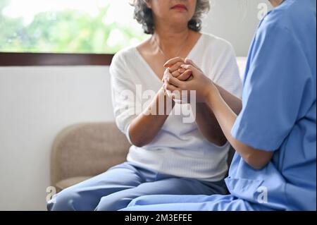 Una dottoressa che tiene le mani di una paziente anziana, offrendo sostegno e comfort durante la riunione. immagine ritagliata e ravvicinata Foto Stock