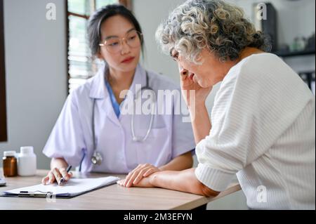 Grave e stressato 60-year-old anziano ritirano la donna che parla, consultandosi con il suo medico nell'ufficio dell'ospedale. Foto Stock