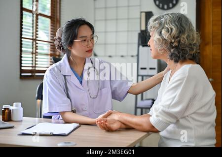 Un medico femminile asiatico premuroso millenario tiene la mano di un paziente per confortare e rassicurare il paziente durante il controllo medico. concetto di assistenza sanitaria Foto Stock