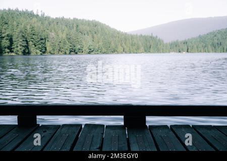 Una parte di una banchina di legno con lo sfondo sfocato del lago Foto Stock