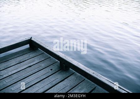 Una parte di una banchina di legno con lo sfondo sfocato del lago Foto Stock