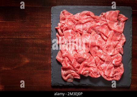 carne giapponese di prima qualità tagliata a fette di manzo o maiale in marmo di Wagyu su ardesia nera su sfondo di legno. Foto Stock