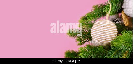 Banner con rami di albero di Natale con ornamento naturale bauble in corda di iuta beige su sfondo rosa Foto Stock