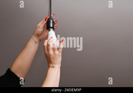 Una donna con belle unghie si avvita in una lampada a LED Foto Stock