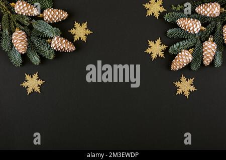 Rami verdi di un albero di Natale con decorazioni in forma di coni dorati e fiocchi di neve su sfondo nero con un posto per il testo. Vista dall'alto Foto Stock