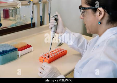 Scienziato donna che pipetta il campione in una fiala in un laboratorio utilizzato per l'analisi chimica e del DNA Foto Stock