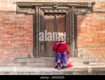 Donna anziana seduta sui gradini di un edificio storico a Bhaktapur, Nepal Foto Stock