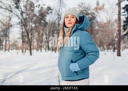 Ritratto di giovane donna che cammina nel parco invernale innevato indossando un cappotto blu. Abiti caldi per climi freddi. Spazio Foto Stock