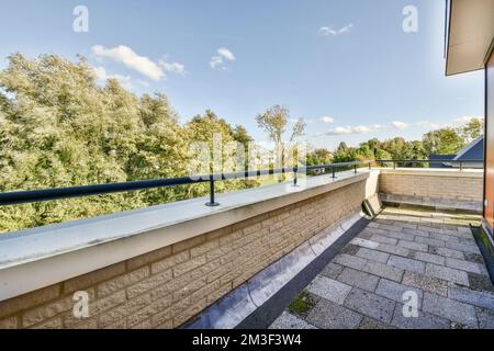 un balcone con alberi e cielo blu sullo sfondo, preso dall'interno di una finestra dell'appartamento che si affaccia sulla strada Foto Stock