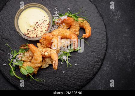 Gamberetti fritti in pastella con salsa, su ardesia nera, su fondo scuro Foto Stock