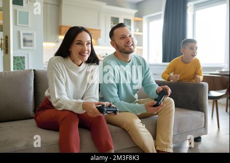 Figlio che guarda mentre madre e padre giocano al videogioco Foto Stock