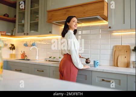 Felice giovane donna cucinare caffè in cezve tazza in cucina Foto Stock